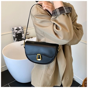 Close-up of black leather saddle bag with gold U-shaped hardware buckle on a model