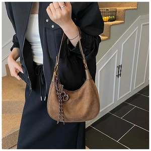 Détail du sac croissant en daim marron mat avec pompon en corde élégant et breloque en métal