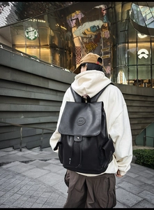 Detailed back view of a large black vintage backpack with drawstring flap and side pockets