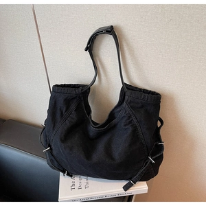 Dettaglio della borsa tote in denim nero con manici in pelle e anelli metallici su libri