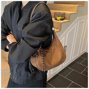 Sac à bandoulière en daim mat marron porté par un mannequin dans un cadre naturel