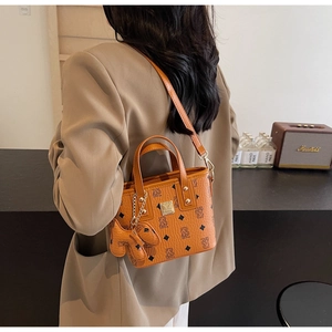 Detail of a brown vintage tote bag with logo pattern, shoulder strap, and dog charm