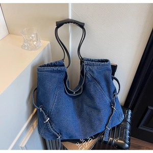 Dettaglio di una grande borsa tote in denim con manici in pelle nera e anelli in metallo