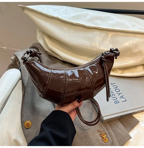 Detail view of dark brown patent leather croissant bag with stylish knotted strap handle