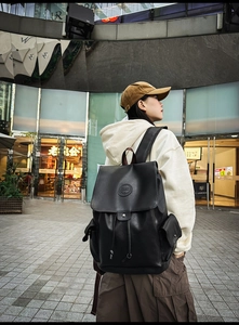 Outdoor street style view of a black vintage backpack with flap and drawstring closure