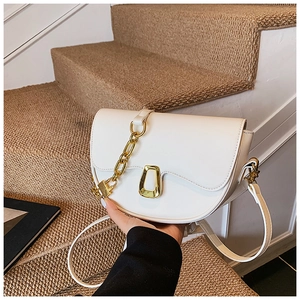 Close-up of beige leather saddle bag with golden metal buckle and decorative thick chain