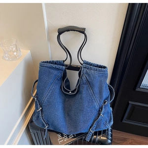 Dettaglio della borsa tote in denim blu scuro con manici in pelle e fibbie in metallo