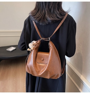 Rear view of brown PU leather backpack with magnetic flap and plush ball charm on a model