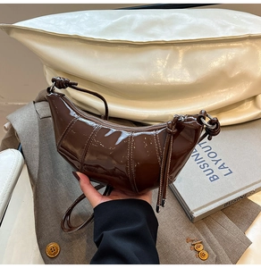 Detail of dark brown patent leather croissant bag with stylish knotted strap design
