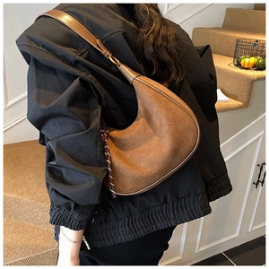 Détail d'un sac hobo en daim marron mat avec cordon, porté à l'épaule pour un style chic
