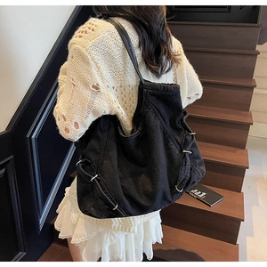 Dettaglio borsa tote nera in denim con anelli metallici indossata su vestito in pizzo bianco