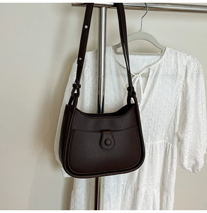 Detail of dark brown pebble leather shoulder bag with buckle flap hanging with dress