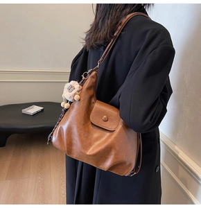 Brown faux leather tote bag with a plush lion charm shown in a minimalist indoor setting