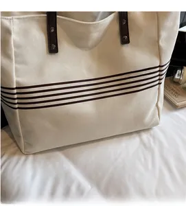 Detail view of canvas tote bag with brown stripes, leather handles and metal rivets