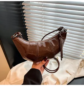 Close-up of brown patent leather croissant bag with quilted texture and knot detail