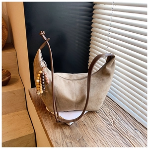 Detail der hobo-Tasche aus Kamel-Wildleder mit Holzperlenanhänger und Lederknoten im Sonnenlicht