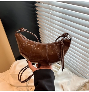 Detail view of brown glossy patent leather croissant bag with knotted shoulder strap