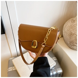 Detail of a brown saddle bag featuring a matte finish and a gold horseshoe buckle closure
