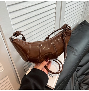 Detailed close-up of a brown patent leather crescent bag with stylish knot strap and silver zipper