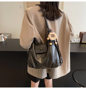 Detail of black leather tote bag with a cute plush sheep charm on narrow strap