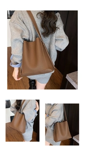 Detail of a large brown pebbled leather bucket bag with an adjustable strap on a model