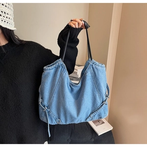 Dettaglio della borsa tote in denim blu con manici in finta pelle nera e fibbie in metallo