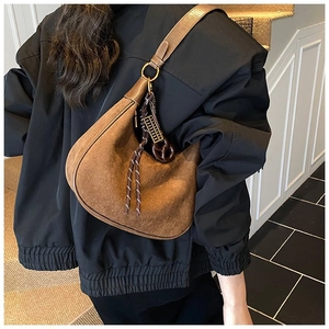 Détail du sac hobo en daim marron avec large bandoulière et décoration de pompon tressé