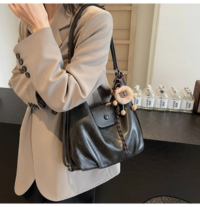 Detail of black PU leather tote bag with pleat texture and plush lion charm accessory