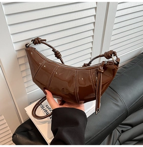 Detail of glossy dark brown patent leather croissant bag with knotted handle and metal zipper