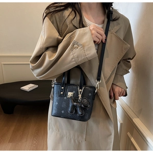Close-up of a black mini tote bag with pattern print and bear charm on khaki coat background