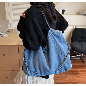 Dettaglio della borsa tote in denim blu con chiusura a coulisse e tracolla in pelle nera