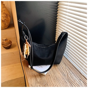 Details einer schwarzen sichelförmigen Canvas-Tasche mit bunter Holzperlen-Quaste im Boho-Stil