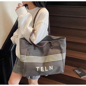 Detail of grey canvas tote bag with brown handles and TELN print on wooden stairs