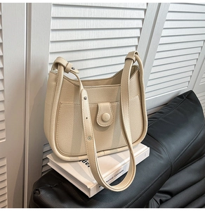 Detail of cream white pebbled leather shoulder bag with buckle pocket on white books