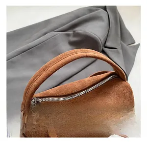Dettaglio ravvicinato della borsa cilindrica in pelle scamosciata marrone con zip