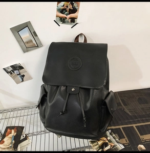 Detail showing the textured black PU leather, circular logo, and drawstring closure of the backpack