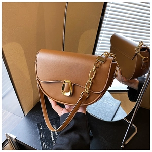 Detail of a brown leather saddle bag with a gold U-shaped buckle and chain strap