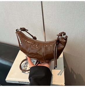 Detail of coffee brown glossy patent leather crescent bag with vertical quilting and silver zipper