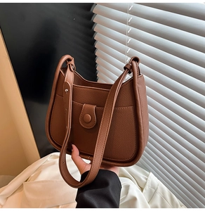 Detail of brown litchi textured leather shoulder bag with round magnetic buckle front pocket