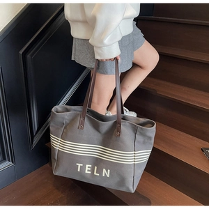 Detail of grey canvas tote bag with leather handles and white logo on wooden stairs