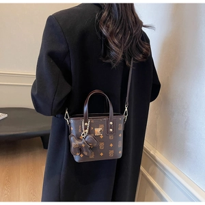 Detail of dark brown monogram mini tote bag with leather bear charm and gold logo plate