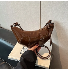 Detailed close-up of dark brown patent leather croissant bag with stylish knotted strap