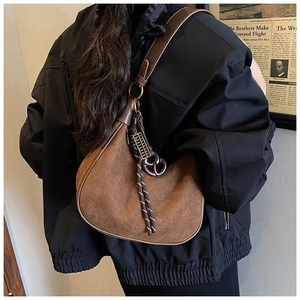 Détail du sac hobo en daim marron foncé avec pompon porté à l'épaule par un mannequin