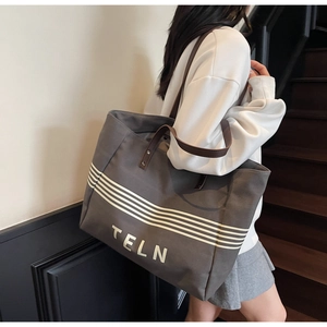 Detail showing the large canvas tote bag with leather straps and TELN print on the shoulder