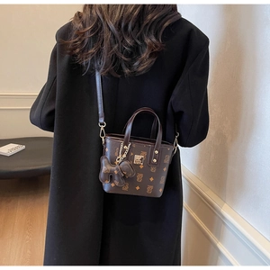 Detailed view of dark brown monogram bucket bag with gold hardware and bear charm