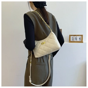 Detail view of white quilted dumpling bag with gold chain strap on model shoulder