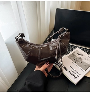 Detailed macro view of dark brown glossy patent leather texture on a crescent bag