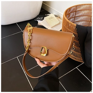 Detail of a brown leather saddle bag with a golden trapezoid clasp and chain strap detail
