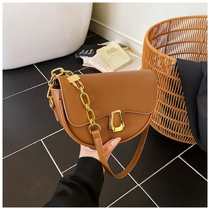 Detail of a brown leather saddle bag with a large gold U-shaped buckle and chain strap
