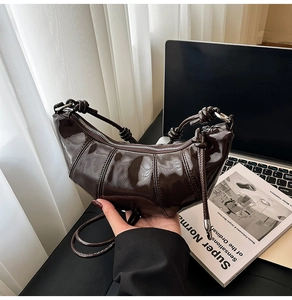 Detail of dark brown patent leather croissant bag with knotted strap and zipper